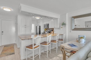 Une cuisine moderne avec des meubles blancs, un îlot central doté de sièges et un coin repas avec une table et des chaises.
