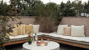 Un espace extérieur accueillant, avec des bancs rembourrés, une table ronde décorée de bougies et une plante en pot.
