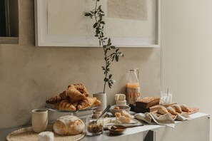 Ein Frühstückstisch mit Gebäck, Brot, Käse und einer Orangensaftflasche.