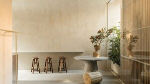 Une pièce au décor minimaliste, avec une table ronde, trois tabourets en bois, un panier tressé et une plante en pot.