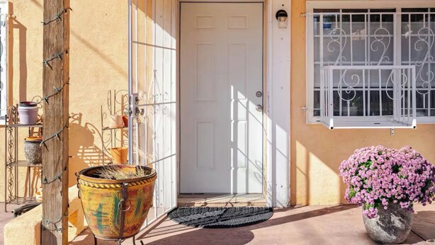 A door with a metal gate, a potted plant with flowers, and a window with a metal grille. - Cozy Casita Albuquerque, New Mexico  (Albuquerque)
