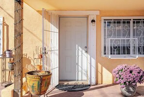 Uma porta com grade de metal, um vaso com flores e uma janela com grades de metal.