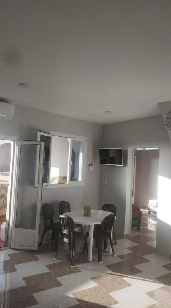 A dining area with a round table and four chairs, a television mounted on the wall, and a checkered floor pattern.