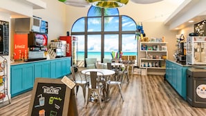 Um café com vista para o oceano, apresentando um quadro de menu, área de estar e diversos pontos de comida e bebida.
