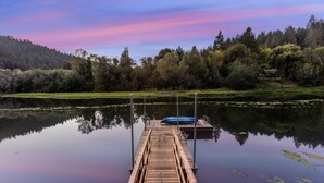 Un muelle de madera se adentra en aguas tranquilas, con un cielo despejado y colinas boscosas al fondo.