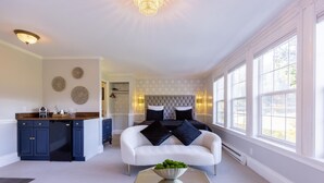 Una sala moderna con un sofá blanco, una mesa de centro de vidrio y una cocina con armarios azul marino y encimera blanca.