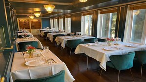 Un restaurante con varias mesas dispuestas para comer, cada una con mantel blanco y sillas verdes.