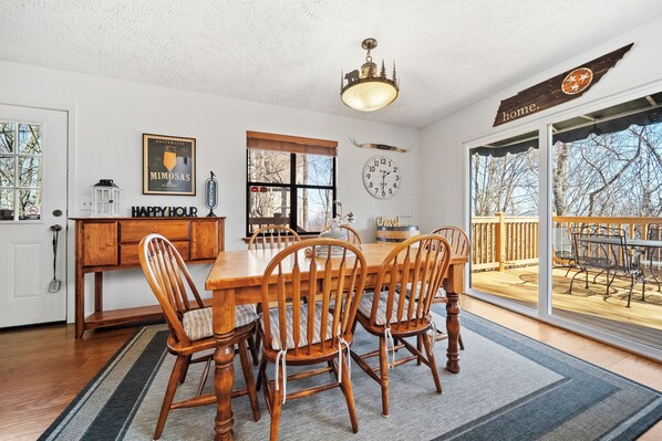 A dining room with a wooden table and chairs, a chandelier, a clock, and a view of the outdoors.