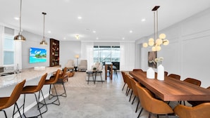 Une cuisine moderne dotée d’un grand îlot central, de tabourets de bar et d’un coin repas avec une table et des chaises en bois.