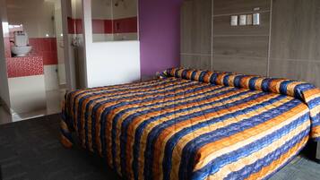 Une chambre d’hôtel avec un grand lit, une salle de bain dont un mur est recouvert de carreaux rouges et blancs, et une tête de lit en bois.