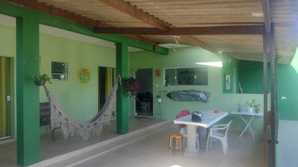 Une pièce avec un mur vert, un hamac, une table avec des chaises et un ventilateur de plafond.