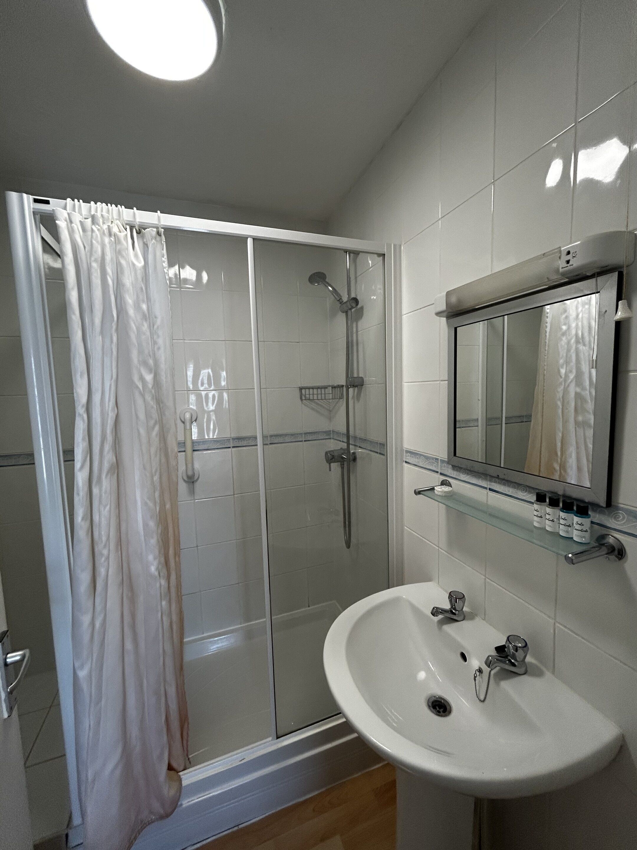 A bathroom with a glass shower enclosure, a white sink, and a mirror above it.