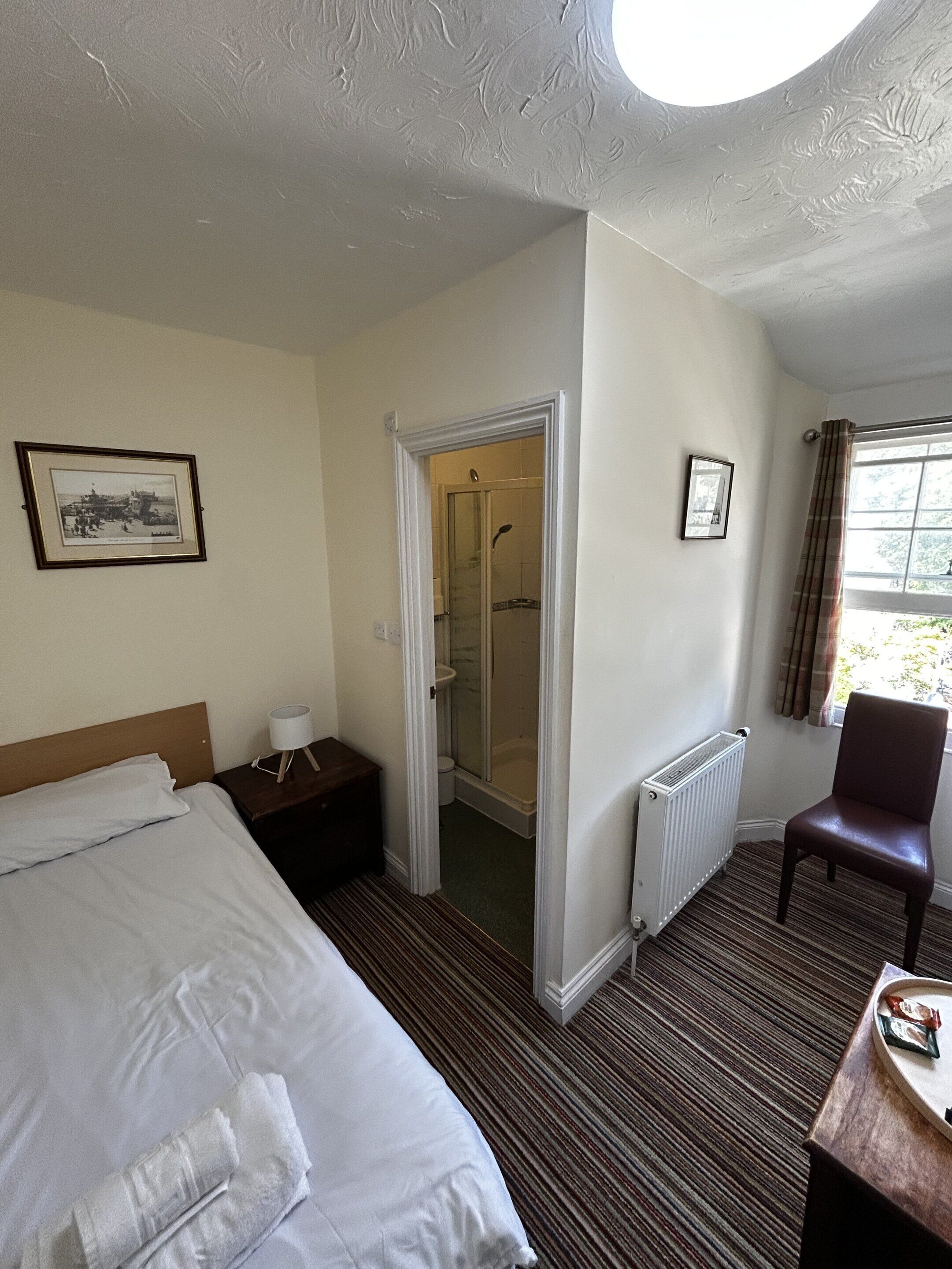 Habitación de hotel con cama, una silla, ducha y radiador.