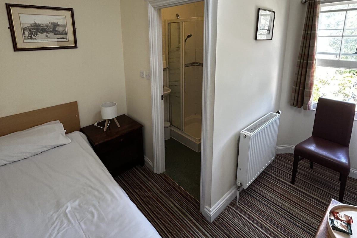 Une chambre d’hôtel avec un lit, une chaise, une douche et un radiateur.