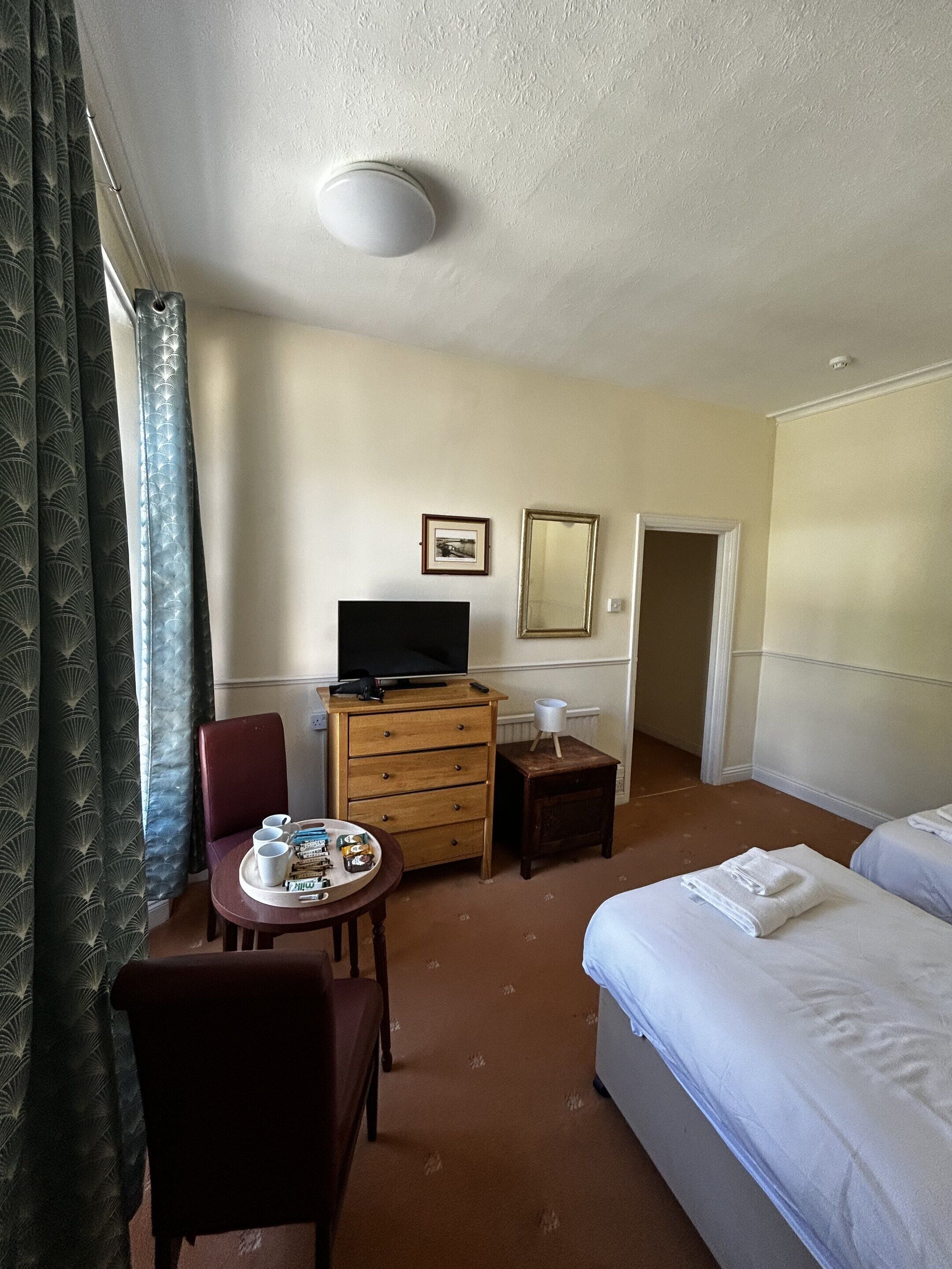 Ein Hotelzimmer mit einem Bett, einem Schreibtisch mit Fernseher, einem Sessel, einem kleinen Tisch mit Gegenständen und einer Tür.
