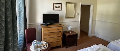 Ein Hotelzimmer mit einem Bett, einem Schreibtisch mit Fernseher, einem Sessel, einem kleinen Tisch mit Gegenständen und einer Tür.
