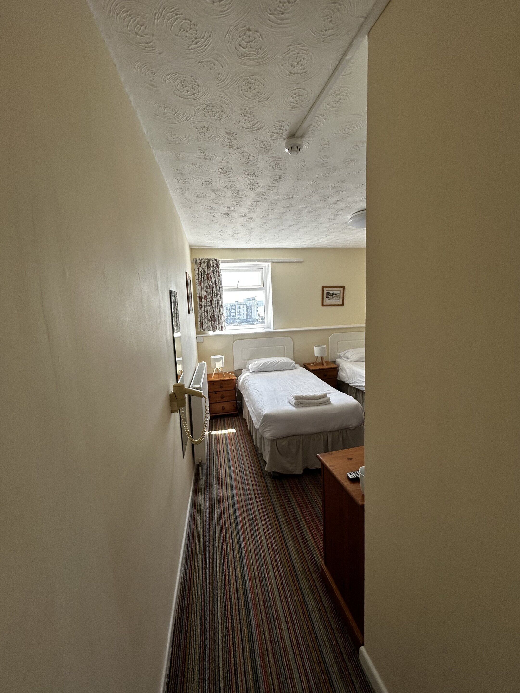 Habitación de hotel con una cama individual, una mesita de noche, cortinas en la ventana y un radiador.