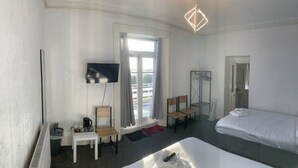 A hotel room with a bed, a TV mounted on the wall, a window with curtains, a radiator, a small table with a kettle and cups, and a hanging coat rack. - Savoy Hotel (Weston-super-Mare)