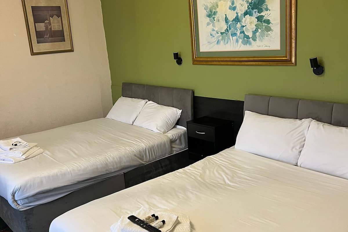 Une chambre d’hôtel avec deux lits, un mur d’accent vert, une œuvre d’art florale encadrée et une petite table sur laquelle se trouvent une télécommande et des articles de toilette.