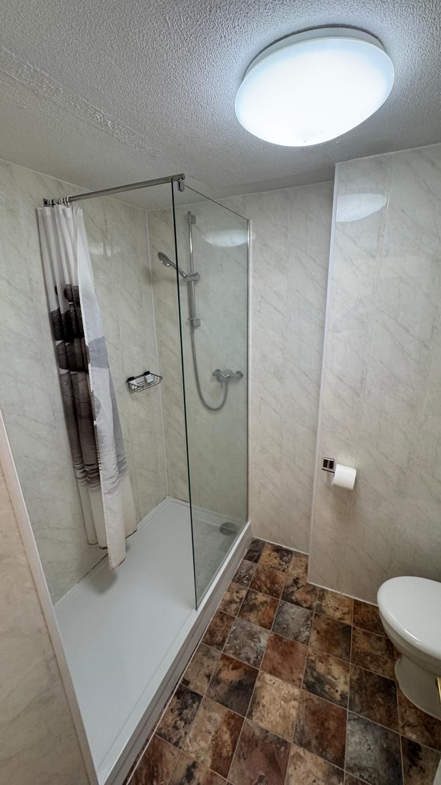 Un baño con ducha acristalada, inodoro y lavamanos.