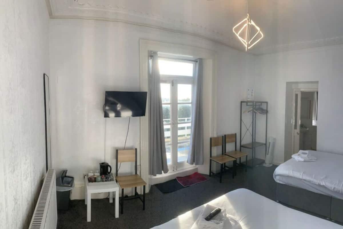 Une chambre d’hôtel équipée d’un lit, d’une télévision, d’un bureau avec une chaise, d’un radiateur et d’une fenêtre avec des rideaux.