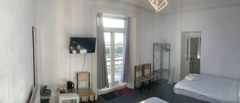 Habitación de hotel con cama, televisión, escritorio y silla, radiador y ventana con cortinas.