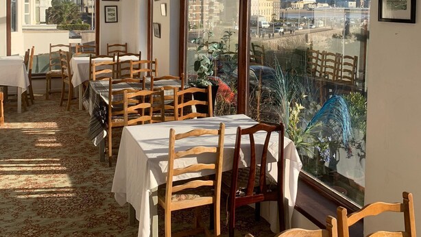 A dining area with tables and chairs, large windows with a city view, and hanging pendant lights. - Savoy Hotel (Weston-super-Mare)