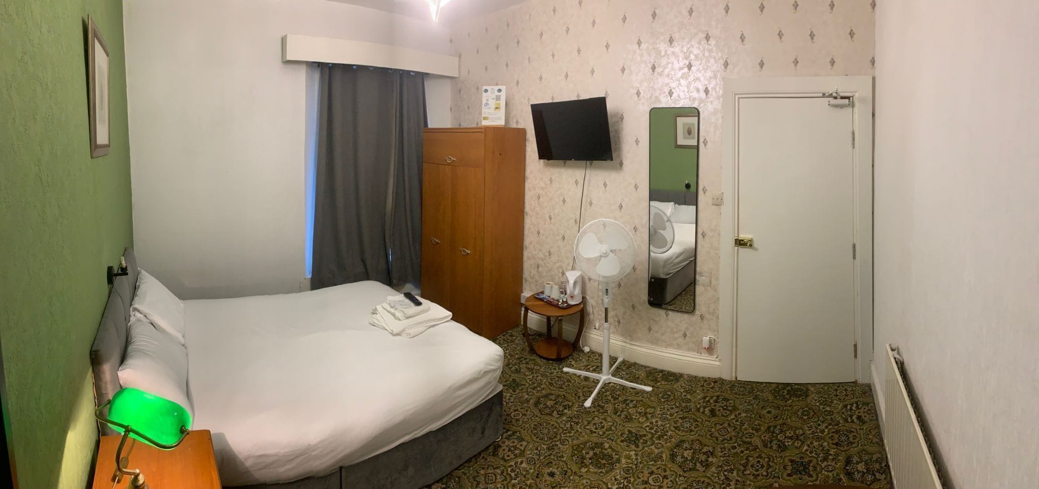 A hotel room with a bed, a desk, a chair, a TV, a mirror, and a wardrobe.