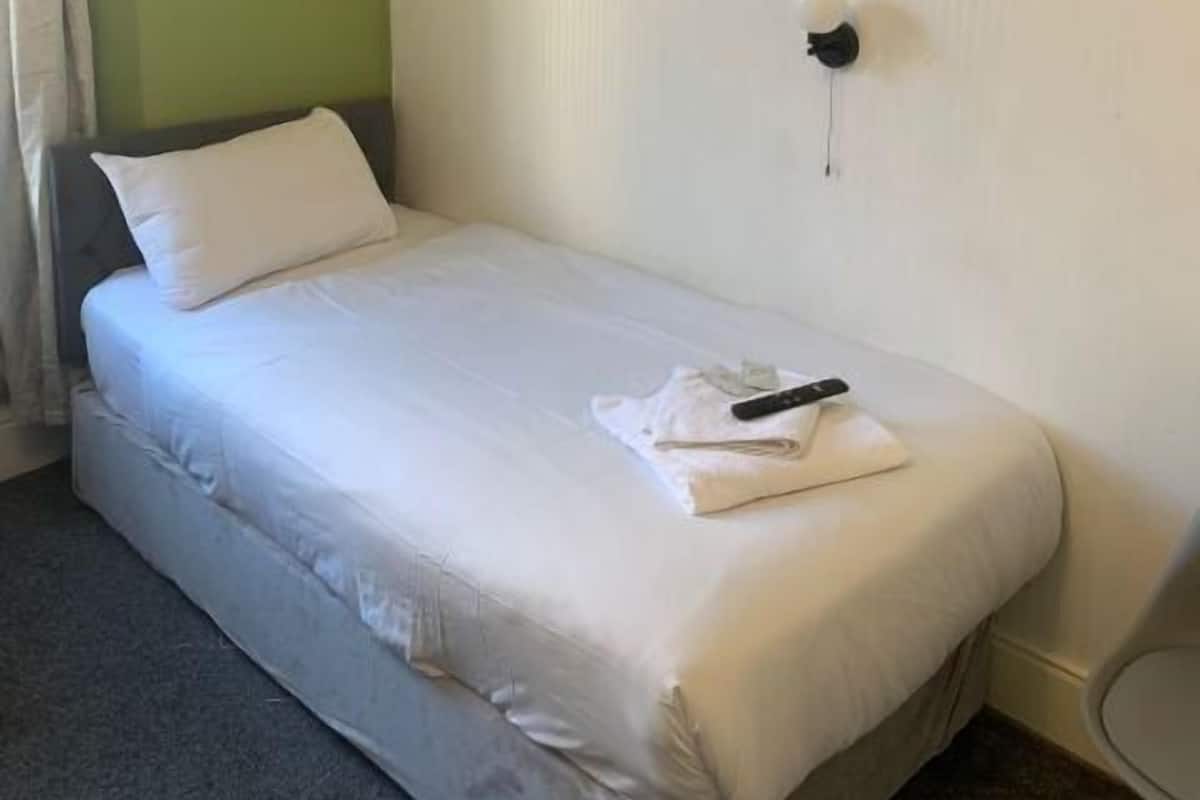 Un lit simple avec une literie blanche, une télécommande et une serviette pliée posée dessus.