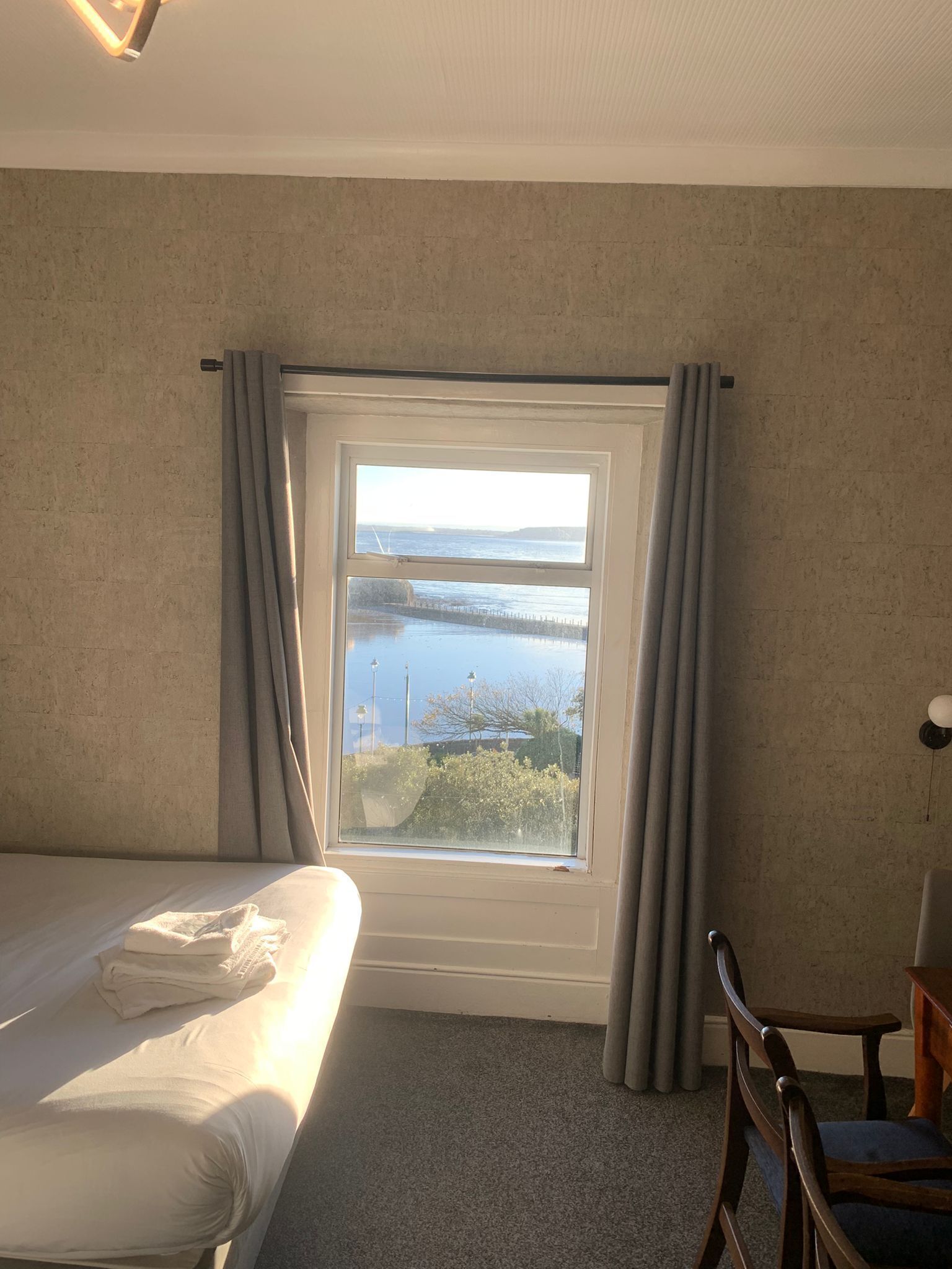 A hotel room with a bed, a view of a body of water, and a chair.