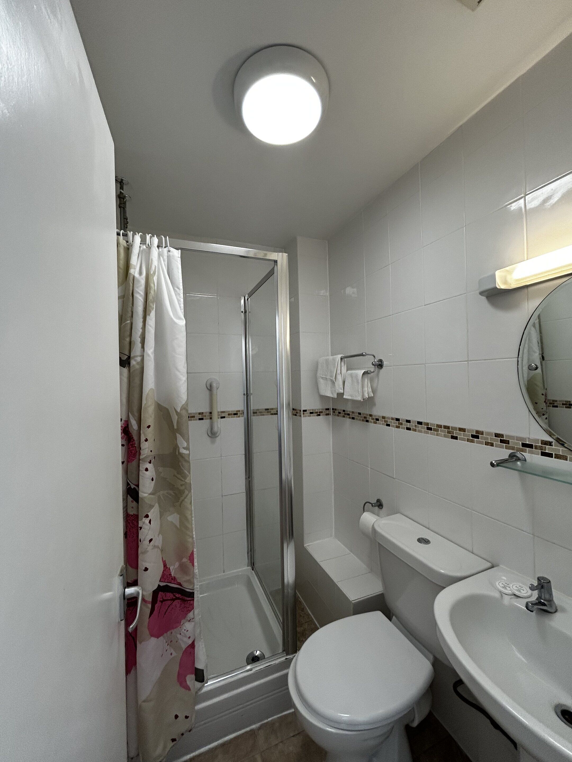 A bathroom with a shower, toilet, and sink, featuring a tiled floor and walls.