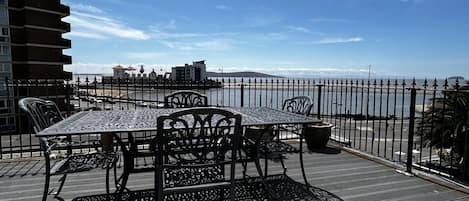An outdoor seating area with a table and chairs, a decorative metal fence, and a view of the sea.