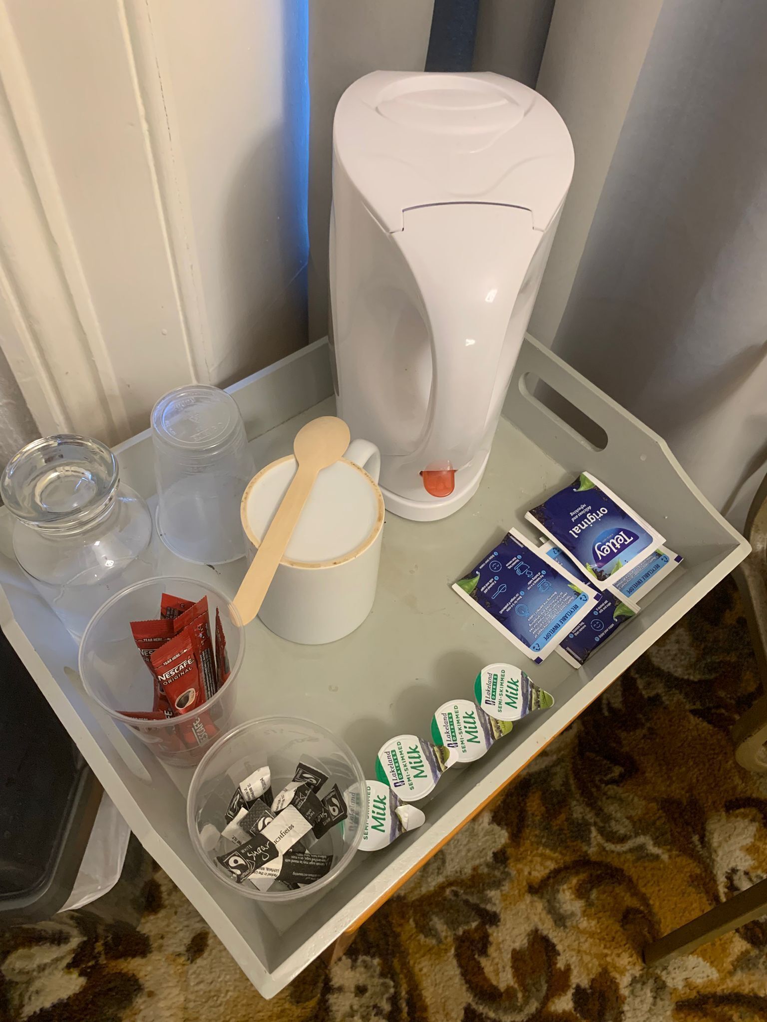 A tray with a coffee maker, a wooden spoon, a cup, and various food items including milk and coffee packets.