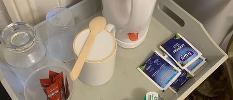 A tray with a coffee maker, a wooden spoon, a cup, and various food items including milk and coffee packets.