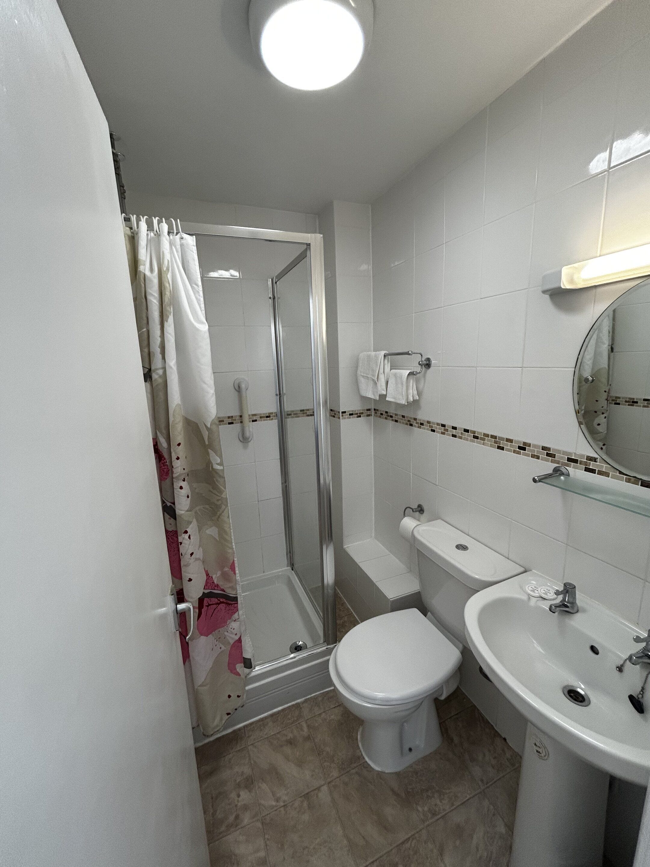 Un baño con ducha, inodoro, lavamanos y un espejo.