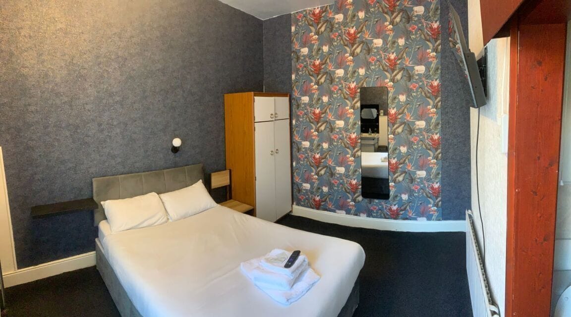 Une chambre d’hôtel avec un lit, une armoire, un miroir et un papier peint à motifs floraux.