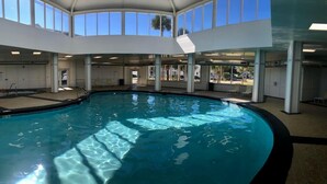 Une piscine intérieure à l’eau claire, entourée de murs très hauts et de grandes fenêtres.