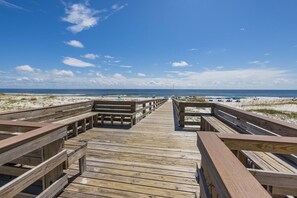 Ein hölzerner Gehweg führt zu einem Strand mit Dünen und blauem Himmel.