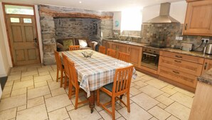A cozy kitchen with a stone wall, wooden cabinets, and a tiled floor. - Tyn Llwyn (Talsarnau)