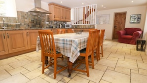 A kitchen with wooden cabinets, a tiled backsplash, a dining table with chairs, and a staircase. - Tyn Llwyn (Talsarnau)