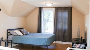 Een slaapkamer met een bed, nachtkastje, televisie en een boekenplank.