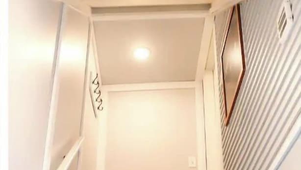 Een trap die leidt naar een kamer met een wit plafond en een raam met horizontale zonwering.