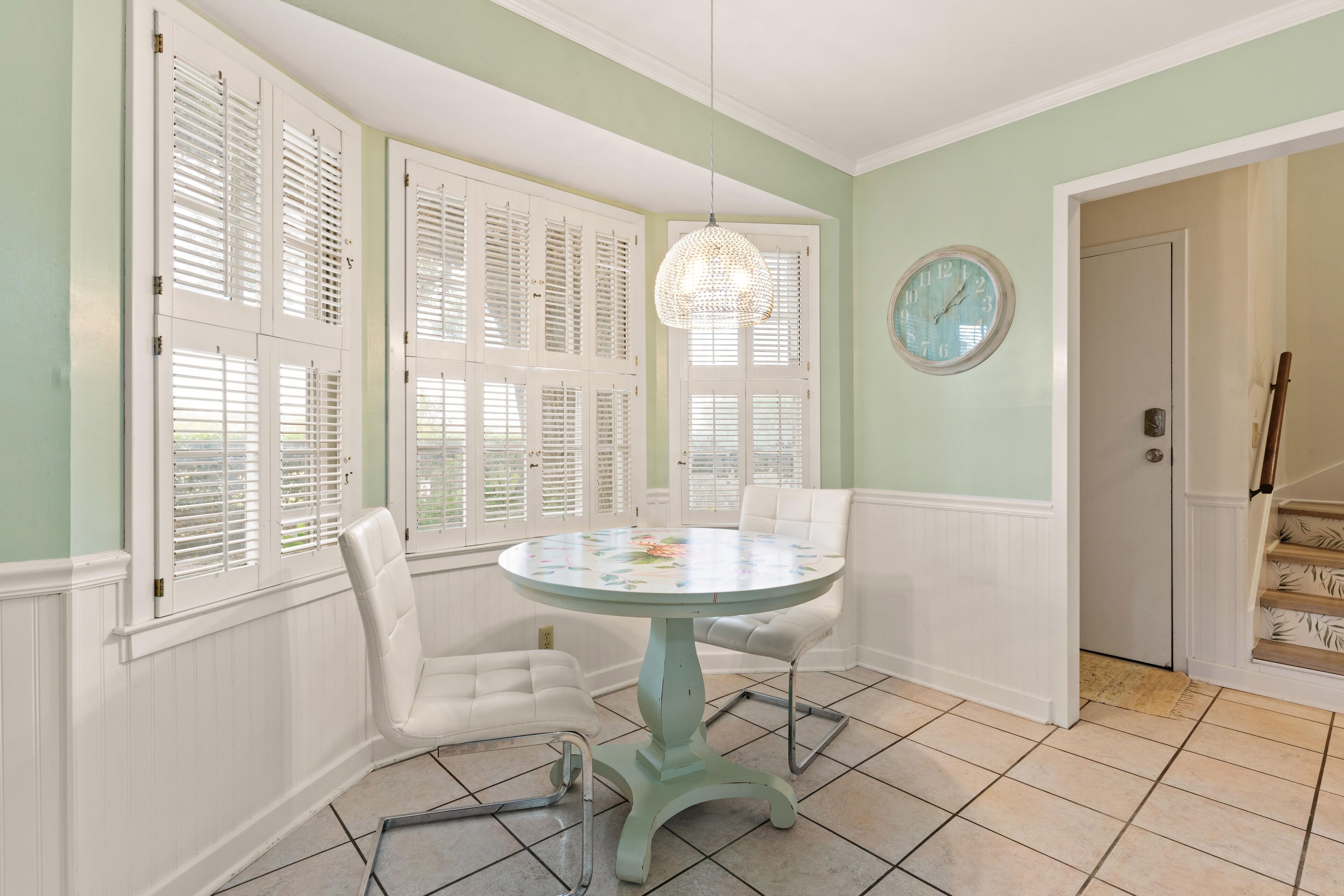 A dining area with a round table, white chairs, and a hanging light fixture.