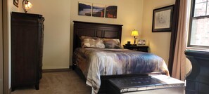 A bedroom with a bed, a nightstand, a lamp, a dresser, and a window.