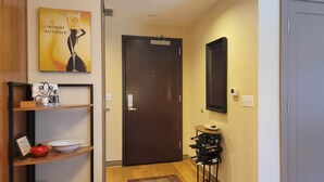 A hallway with a wooden door, a shelf with a wine bottle, a framed picture, and a small table with a bowl. - Beautiful Space in the Heart of NW Portland's Alphabet District (Portland)