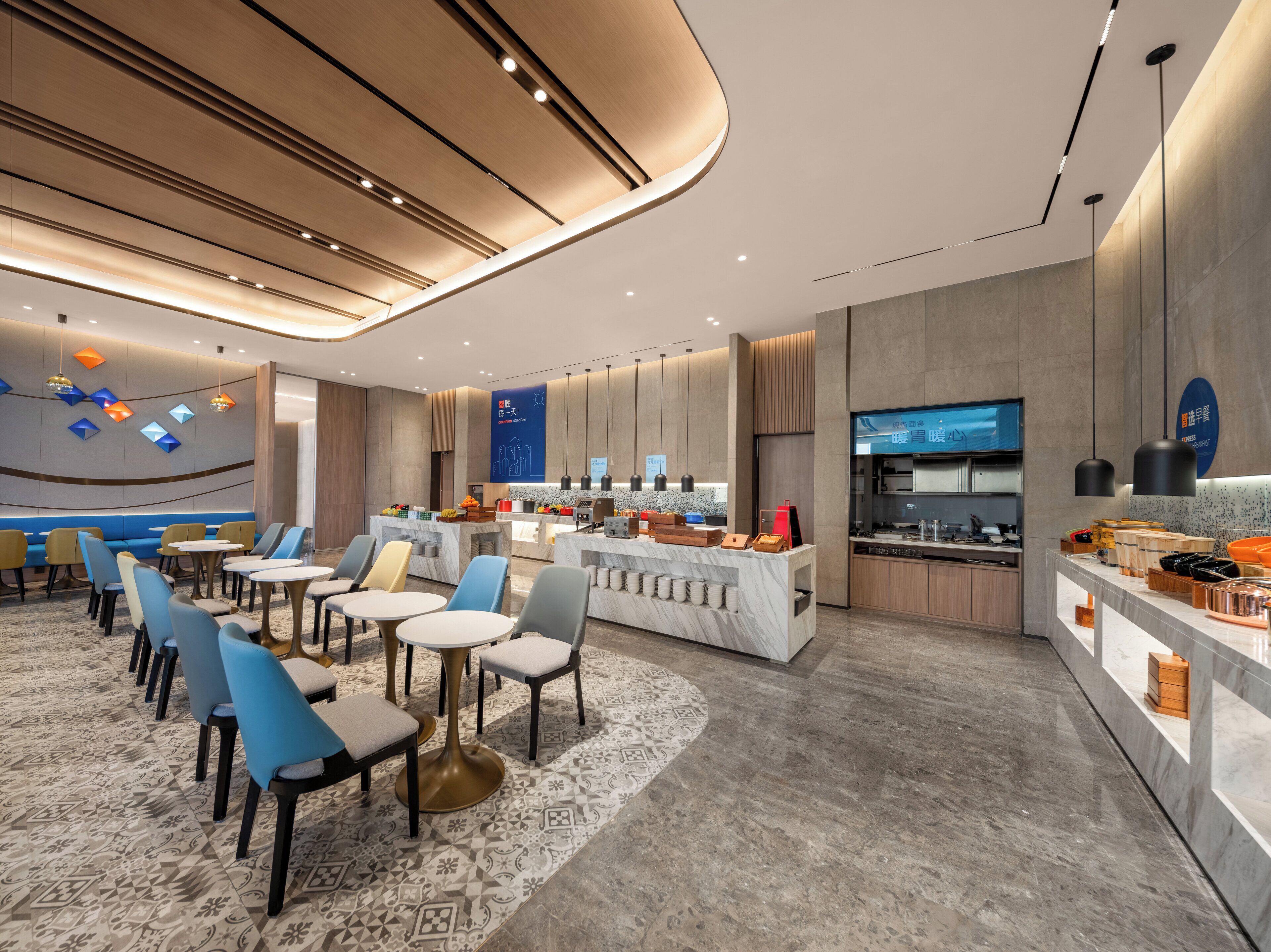 A modern hotel lobby with seating areas, a bar, and a kitchen visible in the background.