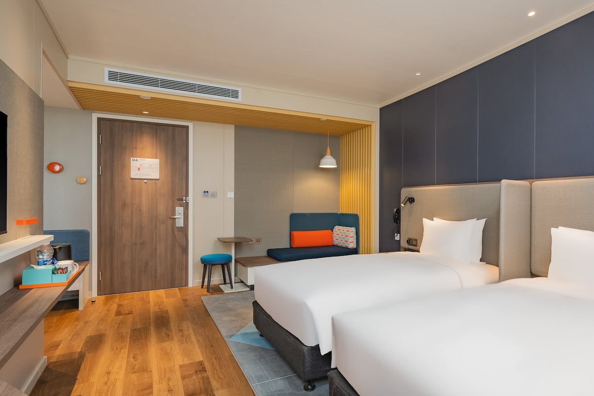 A hotel room with two beds, a TV, a desk, and a small seating area.
