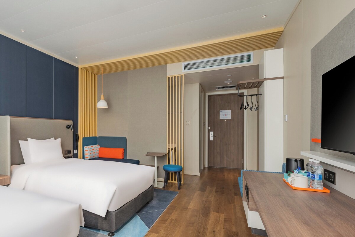 A hotel room with two beds, a desk, a TV, and a bathroom visible through an open door.