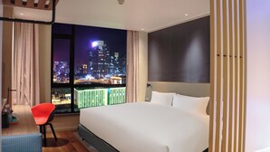 Ein modernes Hotelzimmer mit einem großen Bett, Blick auf die Stadt, einem Essbereich und einem Balkon.
