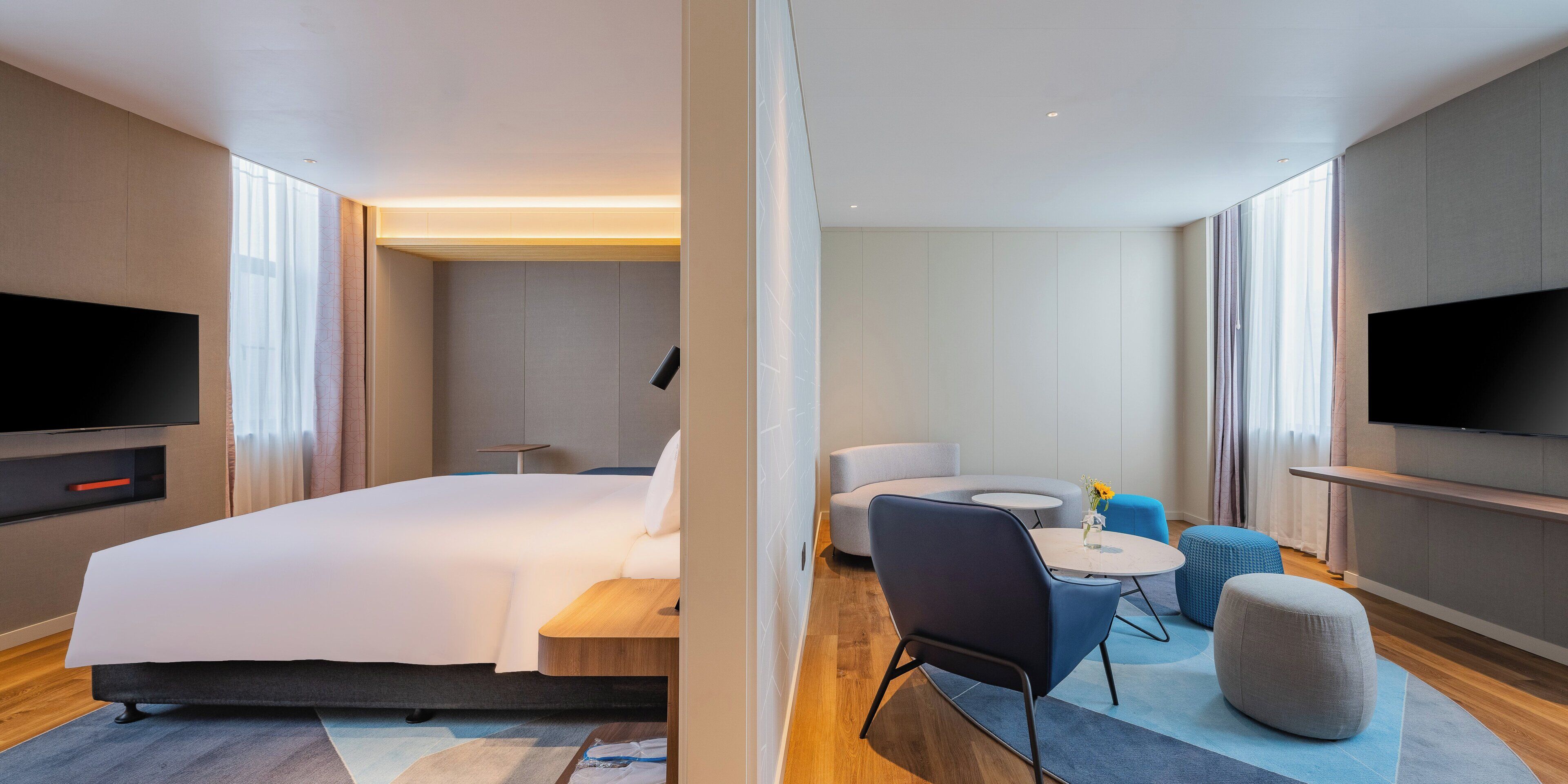 A hotel room with a bed, a TV, a sofa, a small table, and a chair.